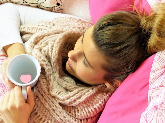 Nemocná žena ležící v posteli pijící čaj