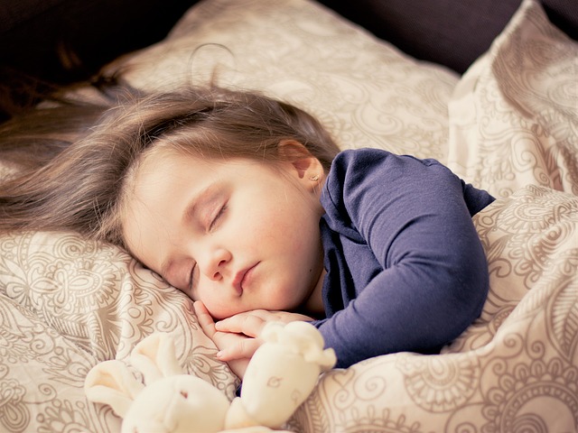 Malá spící holčička v posteli s plyšákem
