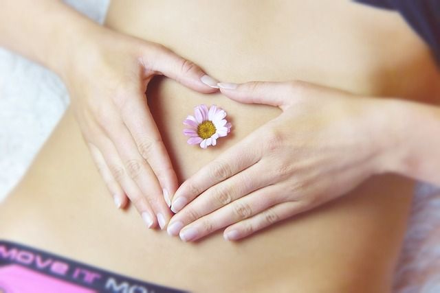 Břicho mladé dívky, ruce ve tvaru srdíčka s květinou uprostřed