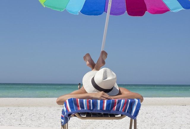 Žena na lehátku na pláži pod slunečníkem